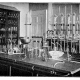 Black and white image showing old fashioned glass testing equipment, bunsen burners etc