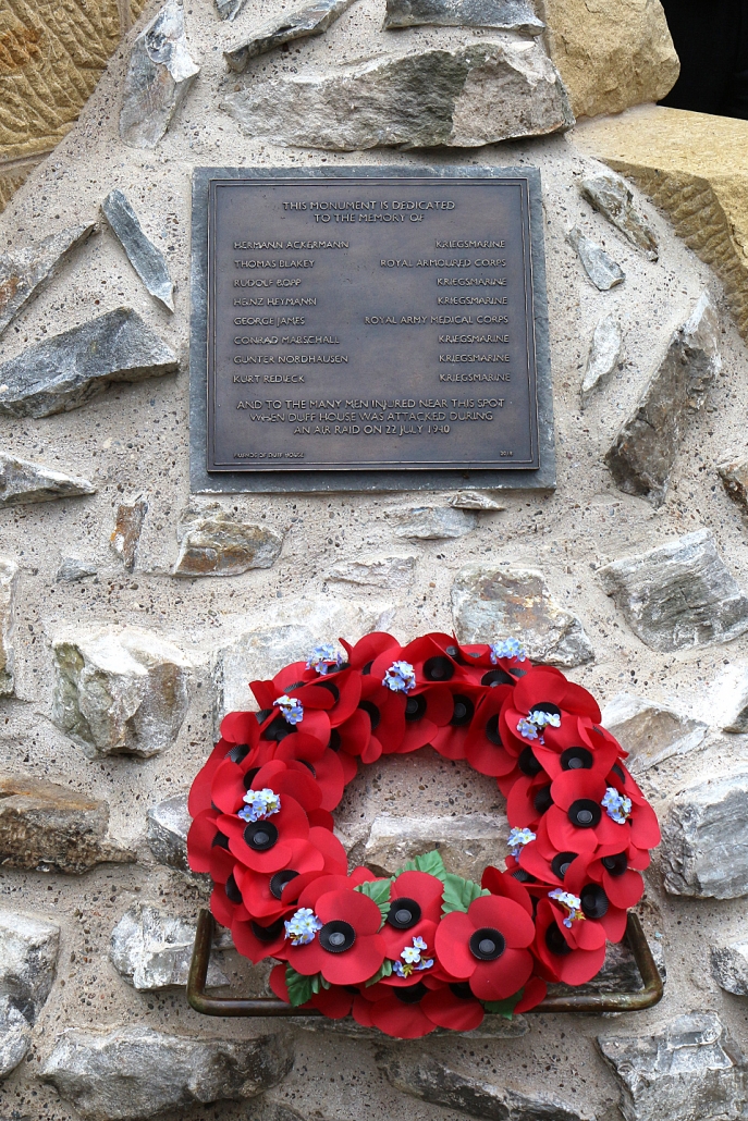 Colour photo of bronze plaque and wreath on a stone background
